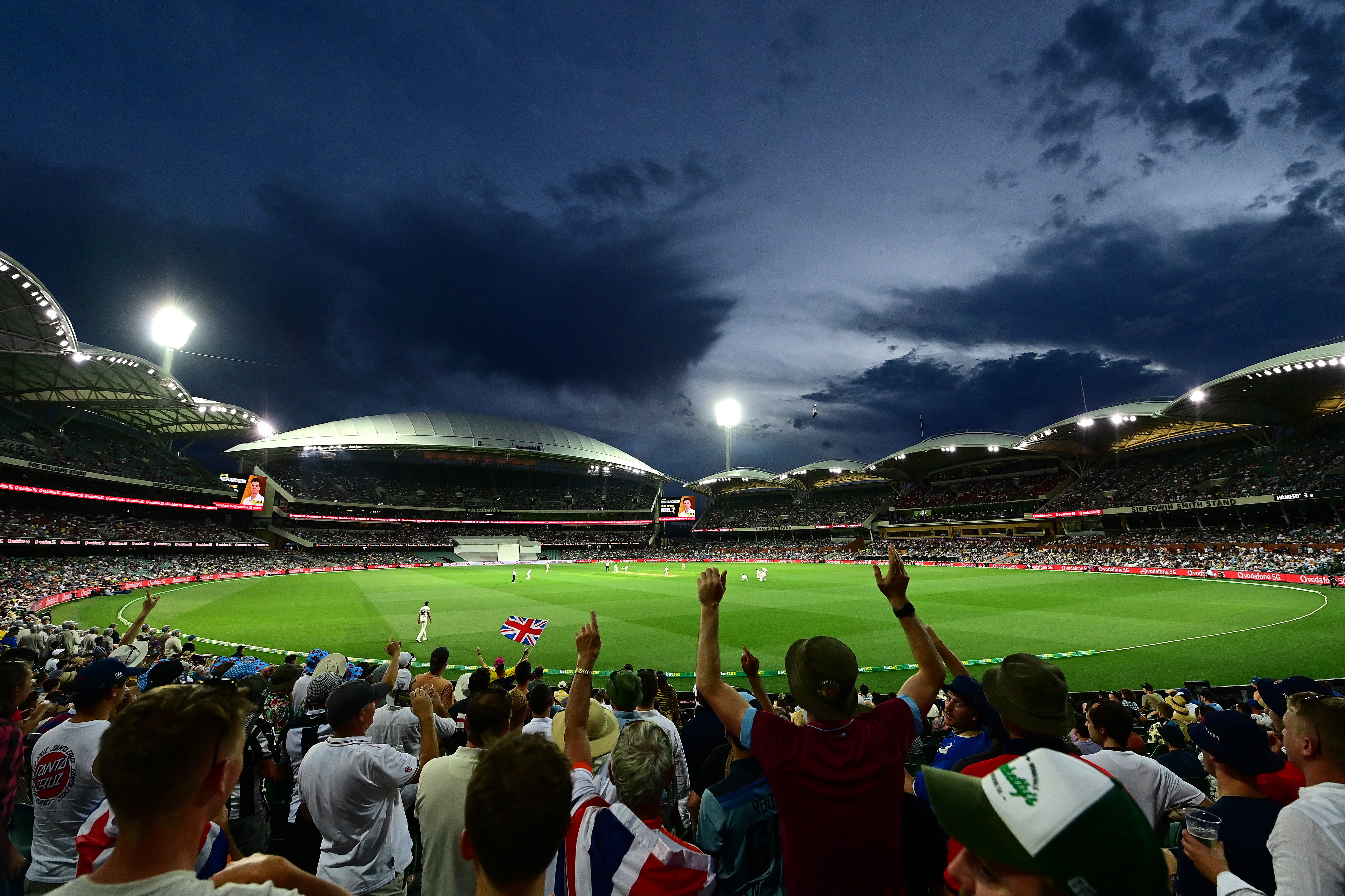 crowd cheering on the cricket players on the green pitch of adelaide oval